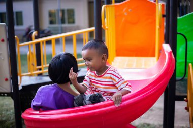 Neşeli çocuklar güneşli bir öğleden sonra oyun parkında kayıyor.