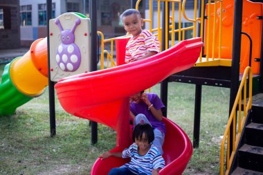 Neşeli çocuklar güneşli bir öğleden sonra oyun parkında kayıyor.