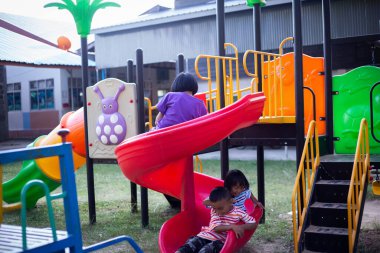 Neşeli çocuklar güneşli bir öğleden sonra oyun parkında kayıyor.