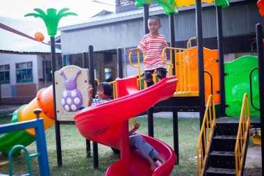 Neşeli çocuklar güneşli bir öğleden sonra oyun parkında kayıyor.