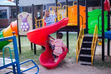 Neşeli çocuklar güneşli bir öğleden sonra oyun parkında kayıyor.