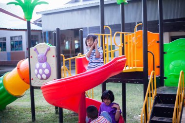 Neşeli çocuklar güneşli bir öğleden sonra oyun parkında kayıyor.