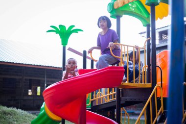 Neşeli çocuklar güneşli bir öğleden sonra oyun parkında kayıyor.