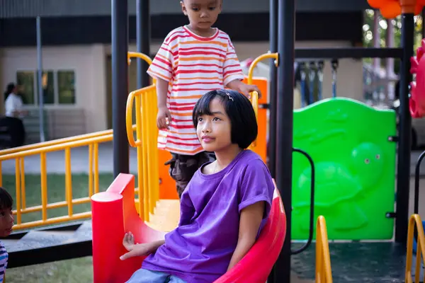 Neşeli çocuklar güneşli bir öğleden sonra oyun parkında kayıyor.