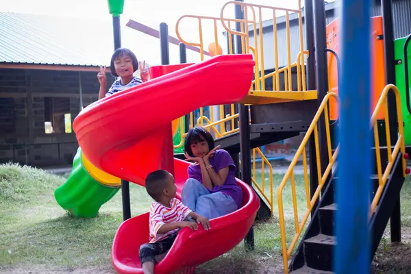 Neşeli çocuklar güneşli bir öğleden sonra oyun parkında kayıyor.