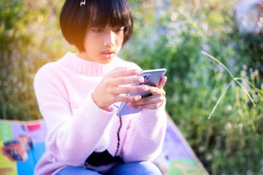 Sevimli küçük kız akıllı telefon kullanıyor. arka planda çim. Kız üzerinde bir balkabağı ile bir saç tokası