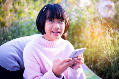 Sevimli küçük kız akıllı telefon kullanıyor. arka planda çim. Kız üzerinde bir balkabağı ile bir saç tokası