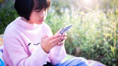 Sevimli küçük kız akıllı telefon kullanıyor. arka planda çim. Kız üzerinde bir balkabağı ile bir saç tokası