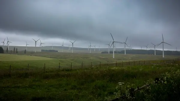 stock image Windmills generating clean green electricity from wind energy on a heavily cloudy day in the typical Scottish landscape