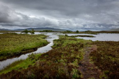Tepeler, dağlar, su, göller, bulutlu gökyüzü ve puslu manzaralı güzel İskoç manzarası.