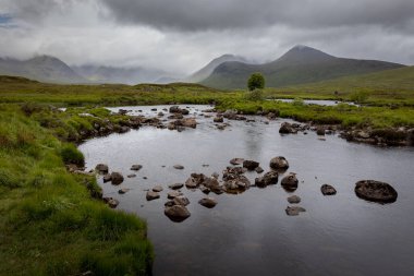 Tepeler, dağlar, su, göller, bulutlu gökyüzü ve puslu manzaralı güzel İskoç manzarası.