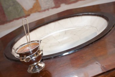 Gümüş vaftiz kepçesi bir kilise ayininde vaftiz fontunun kenarında duruyor.