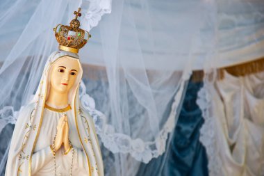 Beyaz bir elbise giyip beyaz bir peçenin altında ellerini bir arada tutan Fatima hanımefendinin heykeli.