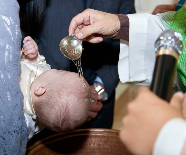 Priest pouring water on a baby's head during a baptism ceremony with family and friends present
