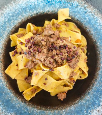 Yaban domuzu ragu soslu pappardelle makarna ve mavi tabakta servis edilen baharatlar, lezzetli bir yemek için mükemmel bir yemek.