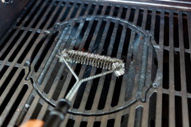 Kirli barbekü ızgarası tel fırçayla temizleniyor.