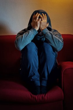 Depresyon ve yalnızlıktan bunalmış bir adam koltukta oturur, zihinsel sağlık sorunlarını yansıtır.