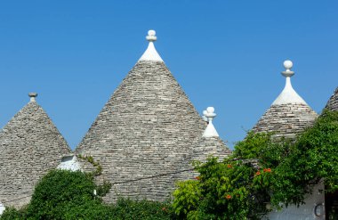 Trulli evlerin geleneksel konik çatıları yığılmış taş levhalardan yapılır ve mavi gökyüzüne karşı beyaz tepelerle süslenir.