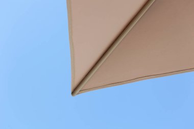 Kumlu bir sahilde, açık mavi gökyüzünün altında, bej rengi plaj şemsiyeleri rahatlama ve koruma çağrıştırıyor. Deniz kenarında rahatlamak için mükemmel.