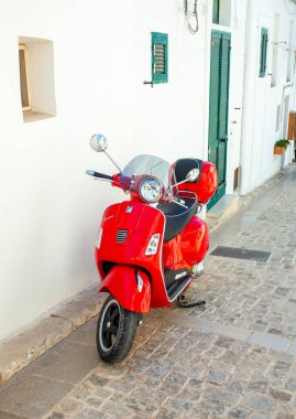 Alberobello, İtalya - 01 Ağustos 2024: Red Vespa Primavera Piaggio bir İtalyan köyünün tipik bir caddesine park etti. Vespa, İtalya 'nın klasik simgelerinden biri haline gelmiş bir scooter..