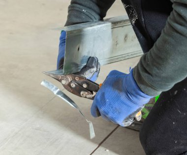 İnşaat işçisi koruyucu eldiven giyip metal bir profili teneke makasıyla kesiyor.