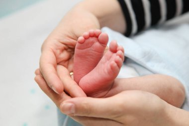 Anne yeni doğmuş bebeğinin ayaklarını elinde tutuyor, şefkatli bir anda sevgi ve ilgi gösteriyor.