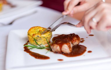 Restoran masasında çatal bıçak kullanan ve soslu domuz filetosu ve patates turtası yiyen bir kadının fotoğrafını çek.