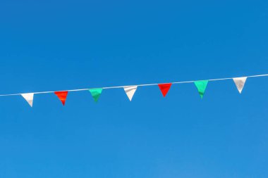 Açık mavi gökyüzüne karşı bir ipte asılı kırmızı, beyaz ve yeşil üçgen bayraklar açık hava düzenine şenlikli bir dokunuş ekliyor. İtalyan bayrağının renkleri.