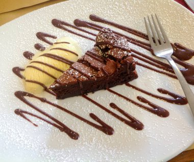 Lezzetli çikolatalı pasta dilimi vanilyalı dondurmayla servis edilir ve beyaz bir tabakta çikolata sosu serpiştirilir, toz şekerle toz haline getirilir.