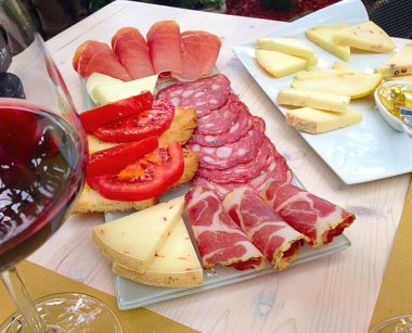 Peynirli, domatesli, jambonlu, salamlı ve bruschetta soslu nefis İtalyan aperatifi bir bardak kırmızı şarapla servis edilir.