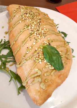 Fıstık ezmesi, fıstık ezmesi ve fesleğen yaprağı ile süslenmiş, beyaz bir tabakta roka ile servis edilen lezzetli bir kızarmış pizzanın kapağı.