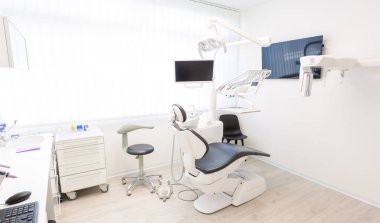 Dişçi koltuğu, monitör ve diğer aletler dahil olmak üzere modern ekipmanları gösteren boş bir diş kliniği hastalar için hazırdır.