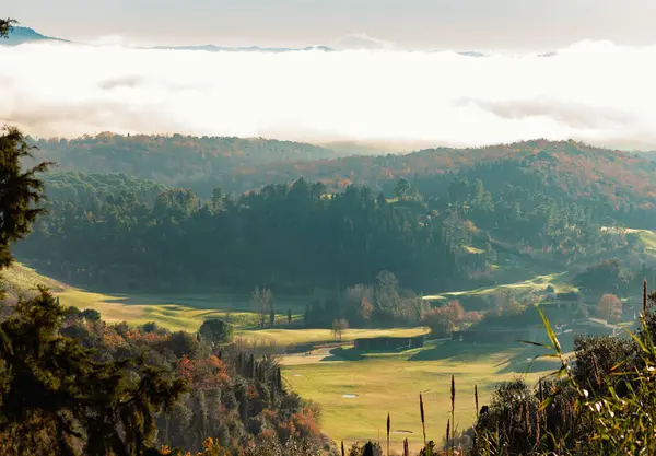 Güneşli bir günün sabahında Castelfalfi yakınlarında bir golf sahasının bulunduğu vadiyi alçak bulutlar kaplıyor.