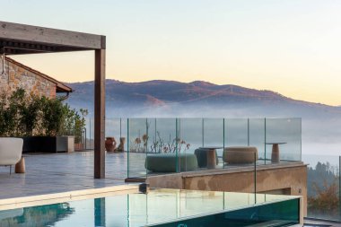 Castelfalfi, İtalya - 15 Aralık 2024: Toskana kırsalında güneş doğarken sisli bir vadiye bakan cam parmaklıklı modern sonsuzluk havuzu