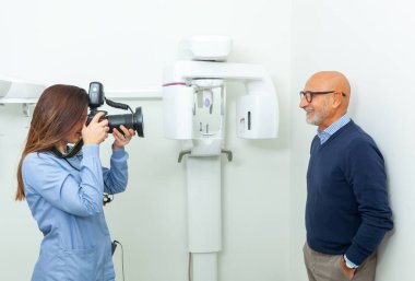 Female dentist taking pictures of smiling senior male patient with professional camera in dental clinic clipart