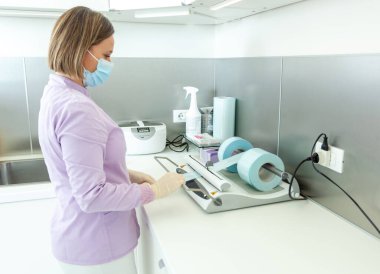 Cerrahi maske ve eldiven takan dişçi hemşireleri otoklav sterilizasyonu için aletler hazırlarken sterilizasyon kesesi mühür makinesi kullanıyorlar.