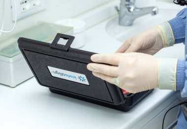 Empoli, İtalya - 19 Aralık 2024: Eldiven giyen dişçi, bir diş sağlığı kliniğinde hastanın ortodonti cihazının bulunduğu Invisalign kutusunu açıyor