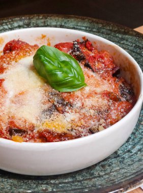 Fesleğen yaprağıyla nefis bir parmesan peyniri, sıcak domates sosu ve kızarmış patlıcan dilimlerini kaplayıp beyaz bir kasede servis et.