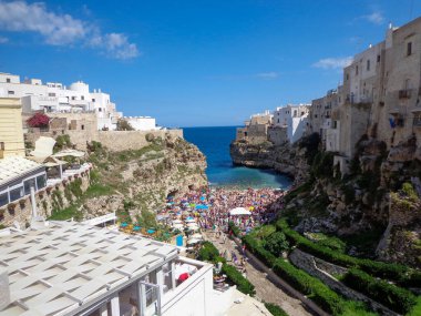 Lama Monachile plajının nefes kesen manzarası, yüksek uçurumların arasına kurulmuş, kristal berrak turkuaz su ve Polignano a Mare, Puglia 'daki canlı yaz atmosferinin tadını çıkaran turistler.