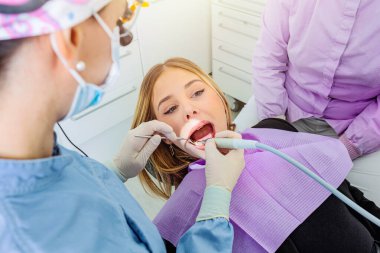 Diş hekimi, dişçi muayenesi için özel aletler kullanan genç bir kadına diş muayenesi yapıyor.