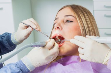 Diş hekimi, dişçi kliniğindeki genç bir bayana yüksek hızlı matkap kullanıyor.