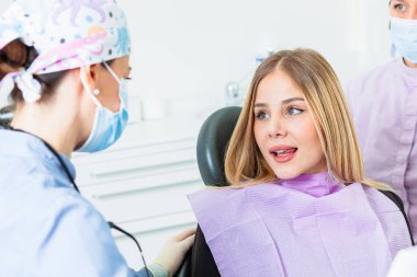 Cerrahi maske takan kadın dişçi. Parlak diş sağlığı kliniğinde hastaların semptomlarını dinliyormuş.