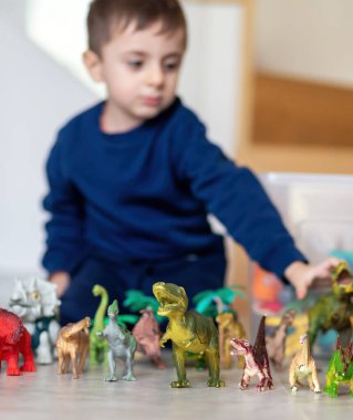 Odasında dinozor oyuncaklarıyla oynayan bulanık bir çocuk, oyuncaklara özenli odaklanma, sığ alan derinliği, parlak renkler, çocukluk kavramı ve oyun.