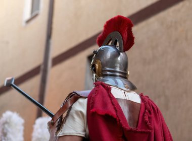 Romalı bir komutan, üzerinde çarpıcı kırmızı bir duman ve akmakta olan kırmızı bir pelerin bulunan bir miğfer takmış, canlı bir tarihi canlandırmaya katılarak kendine güvenen bir mızrak tutuyordu.