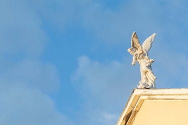 Aziz Mikail 'in beyaz heykeli Şeytanı katlediyor. Mavi gökyüzü ve arka planda bulutlar olan bir kilisenin çatısına yerleştirilmiş.