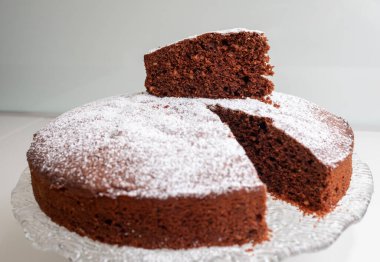 Yuvarlak caprese pasta krema serpiştirilmiş, şeffaf cam pasta standı üzerinde dinleniyor, içine yerleştirilmiş bir kesik ile içindeki yumuşaklığı gösteriyor