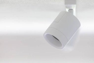 Beyaz bir tavana monte edilmiş silindirik ray aydınlatma armatürü, beyaz bir duvarı aydınlatıyor ve uzayın parlak, modern atmosferini geliştiriyor, çağdaş iç tasarım için mükemmel.