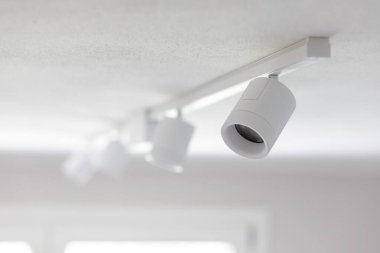 Tavan demirlerinden sarkan beyaz spot ışıkları, parlak bir odayı aydınlatıyor ve zarif sadelik ve çağdaş tasarım elementleriyle modern, şık bir atmosferi geliştiriyor.