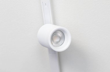 Modern beyaz LED spot ışığı parlak beyaz bir ışık sistemi üzerine monte edildi, el değmemiş beyaz bir duvar parlıyor ve çağdaş iç tasarımda minimalist bir ambiyansı geliştiriyor.