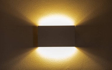 Yukarı ve aşağı doğru sıcak, davetkar bir parıltı saçan modern bir duvar lambası, zarif dokulu bir duvara karşı zarifliği arttırır, iç tasarım ve ev dekorunu zenginleştirir.